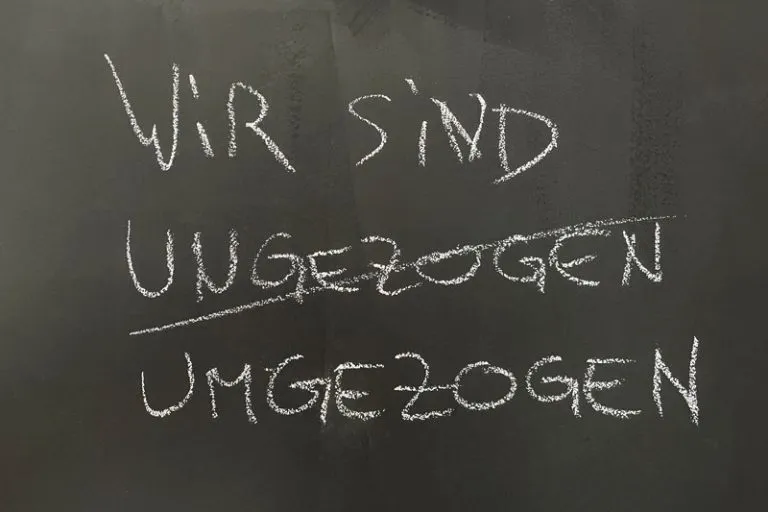 Kreidetafel mit der Aufschrift „Wir sind umgezogen“, das Wort „ungezogen“ durchgestrichen