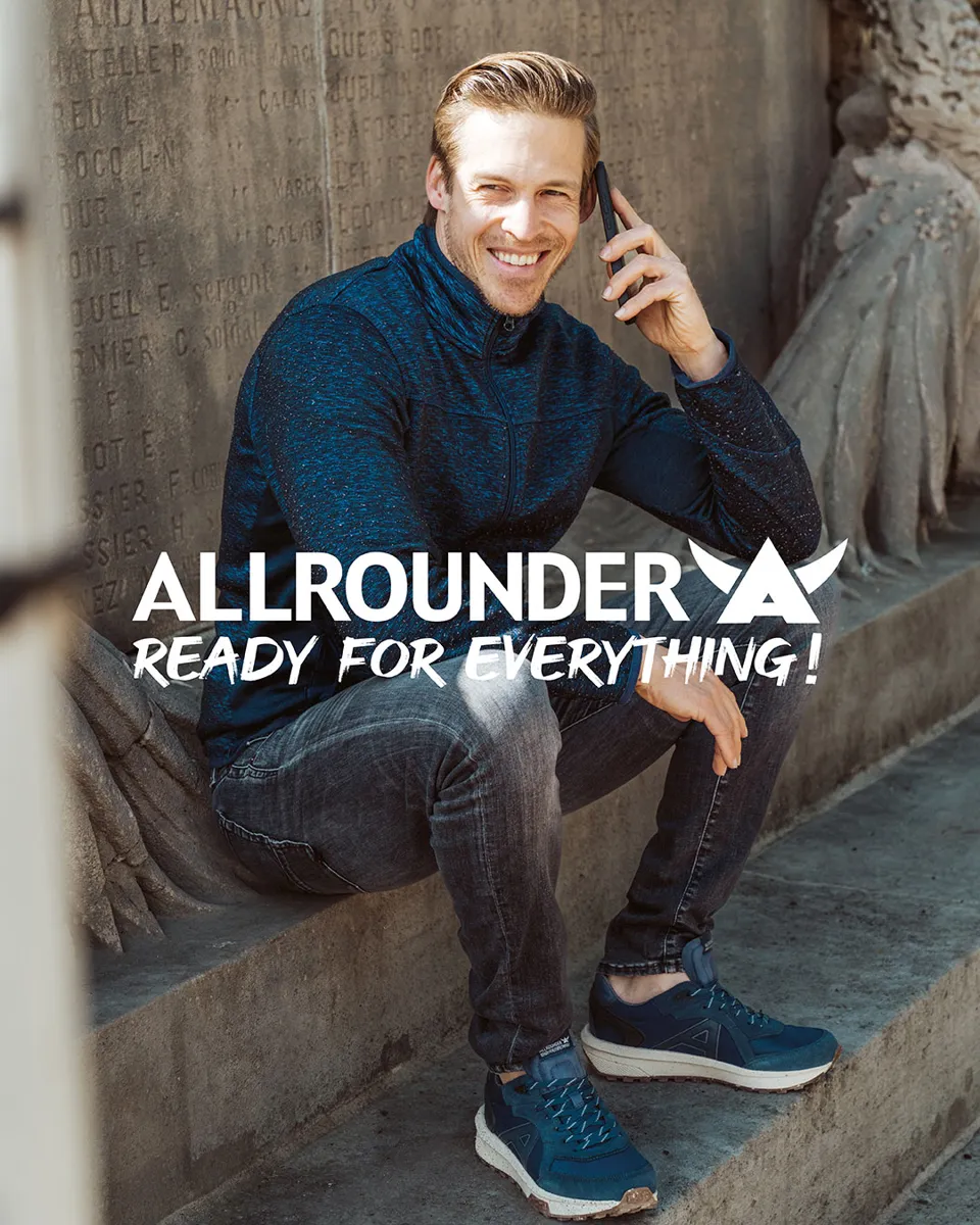 Mann mit Smartphone auf einer Steinmauer, Kampagnenmotiv der Outdoor-Marke Allrounder aus Sarrebourg