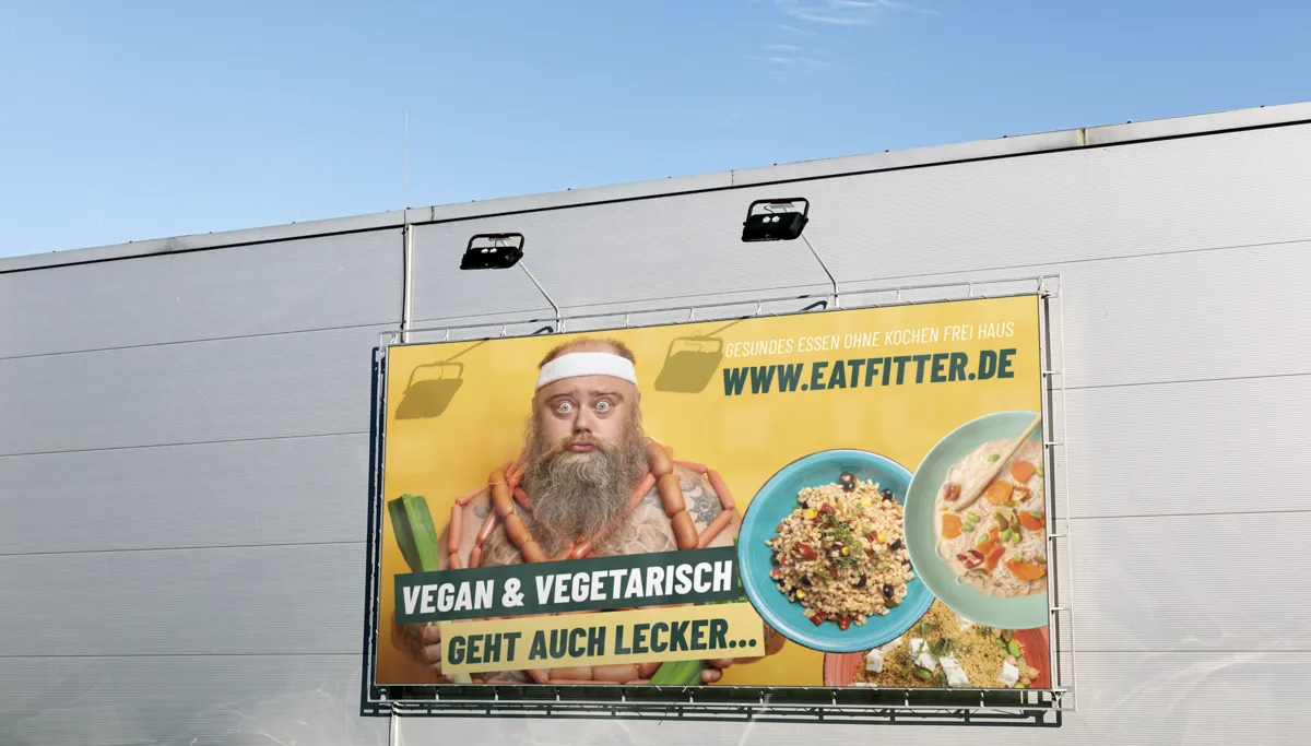 Großflächenplakat von EATFITTER mit bärtigem Mann und vegetarischen Gerichten an einer Hallenwand