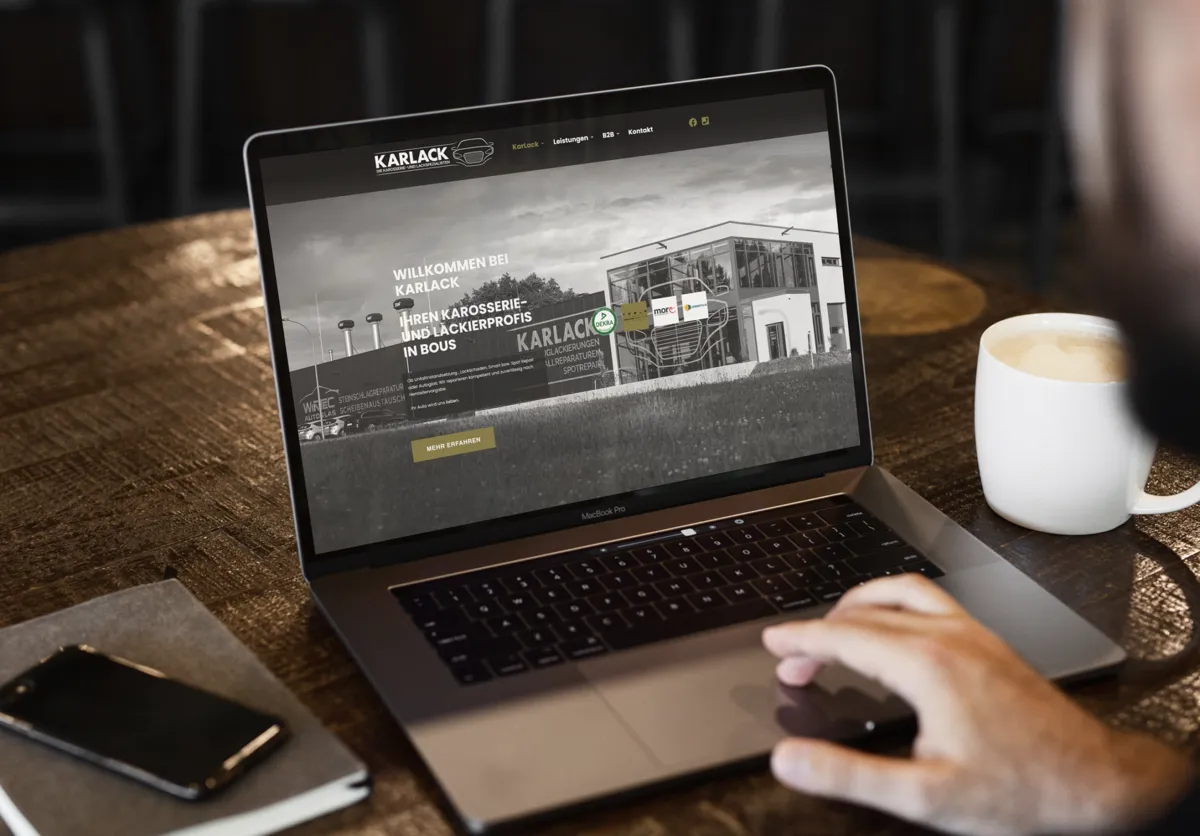 Website von Karlack aus Bous auf einem Laptop auf einem Holztisch mit Kaffeetasse