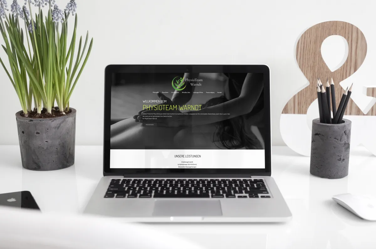 Website des PhysioTeam Warndt auf einem Laptop an einem hellen Schreibtisch mit Pflanze