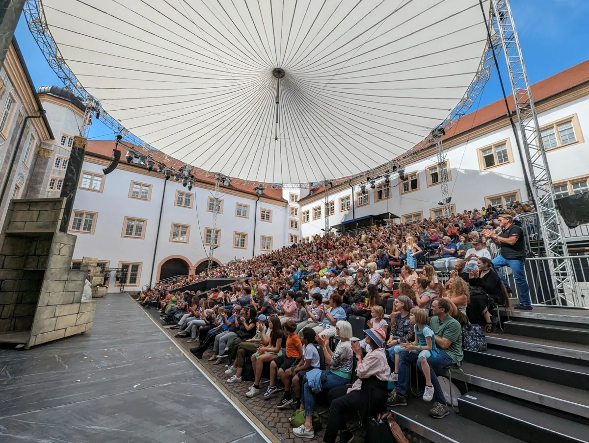 Voll besetzte Zuschauertribüne unter dem Zeltdach der Schlossfestspiele Ettlingen im Schlosshof