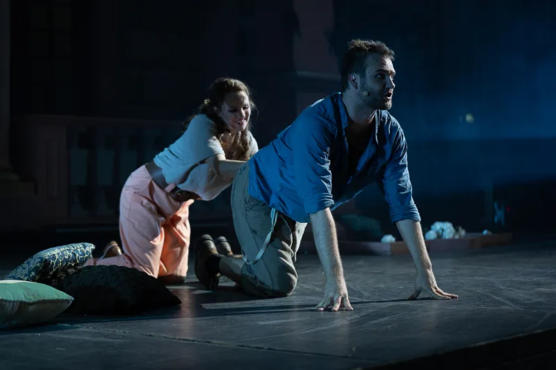 Szenenfoto der Schlossfestspiele Ettlingen: zwei Schauspieler knien auf der dunklen Bühne