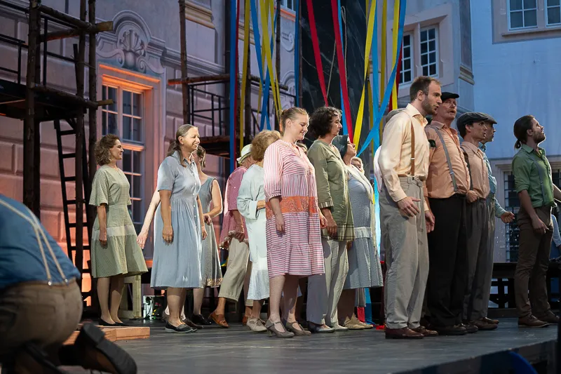 Ensemble in historischen Kostümen auf der Bühne der Schlossfestspiele Ettlingen vor bunten Bändern