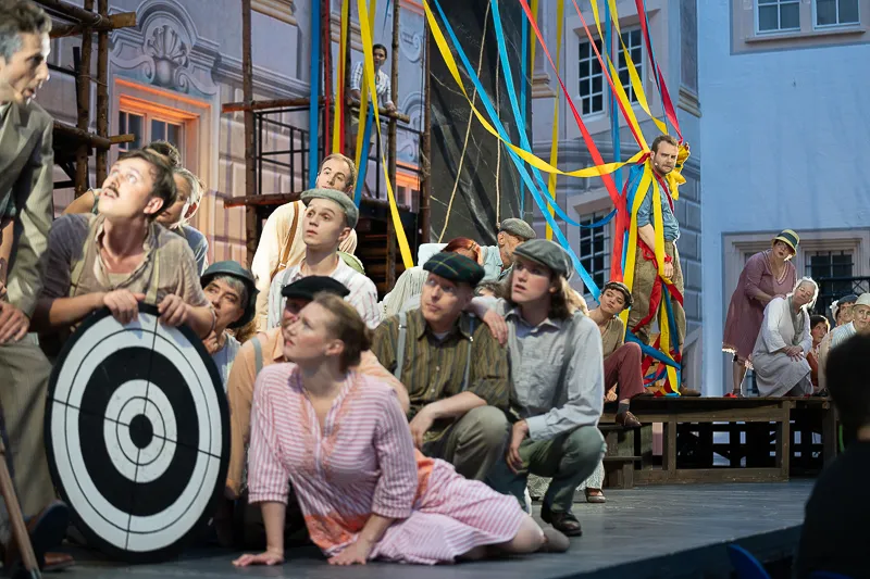 Schauspielerinnen und Schauspieler drängen sich um eine Zielscheibe, Szene der Schlossfestspiele Ettlingen