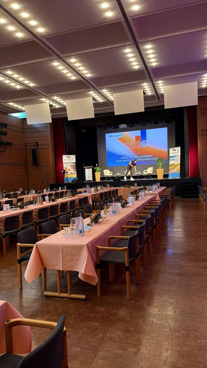 Eingedeckter Saal mit Bühne und Leinwand vor der Vertreterversammlung der levoBank