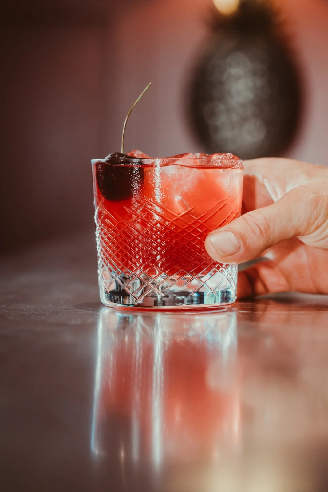 Getränkefotografie: roter Cocktail mit Eis und Kirsche im Kristallglas auf spiegelnder Bar