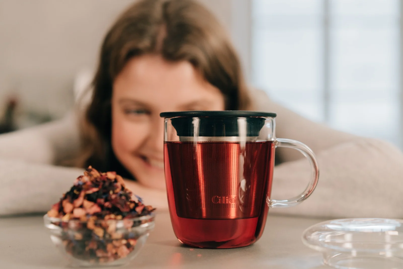 Produktfotografie für Cilia: lächelnde Frau hinter einer Teetasse mit Tee und losen Teeblättern