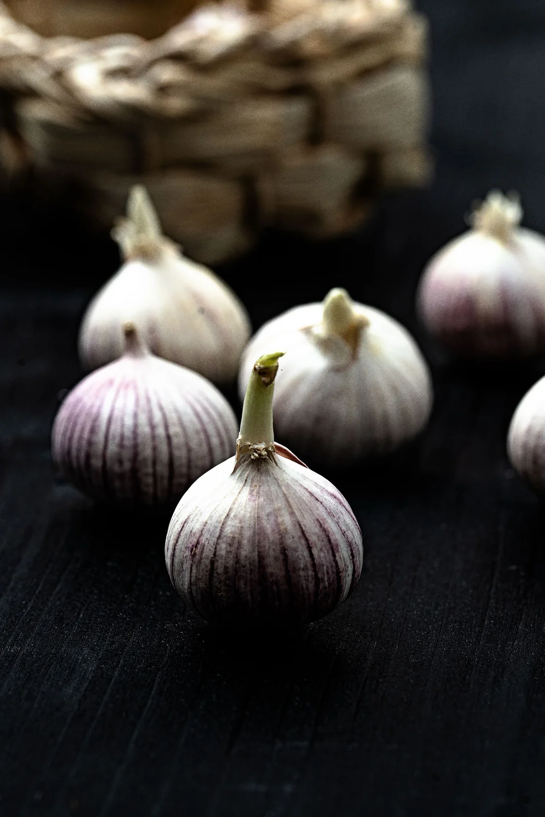 Foodfotografie: Knoblauchknollen auf dunklem Holz vor einem Korb