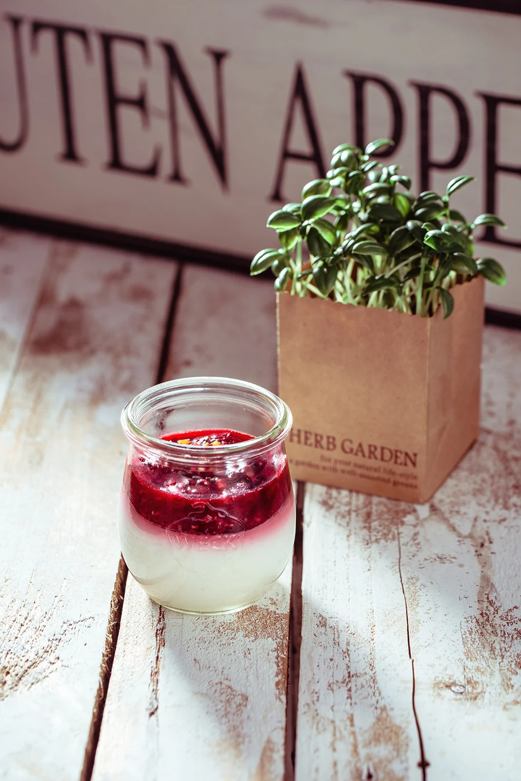 Foodfotografie: Panna cotta mit roter Fruchtsoße im Weckglas neben Kräutertopf