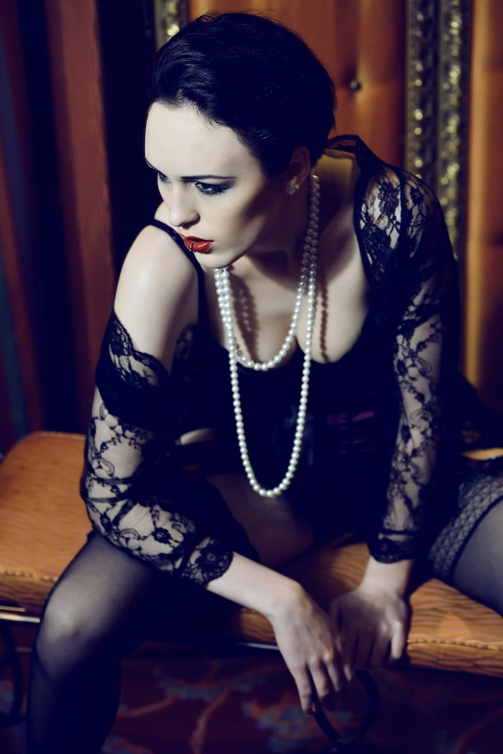 Fashion-Shooting: Model in schwarzer Spitze mit langer Perlenkette auf einer Bank